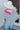 Back view of model wearing the Around The Block Sweater, which features grey knit fabric with pink colorblock details on the wrist and neckline, a v neck and back, and long sleeves.