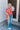 Full body front view of model wearing the Feeling Fine Top, which features a brown, pink, and orange swirl print, a high neckline, half-length sleeves, and a flowy fit. Shirt styled with front tuck