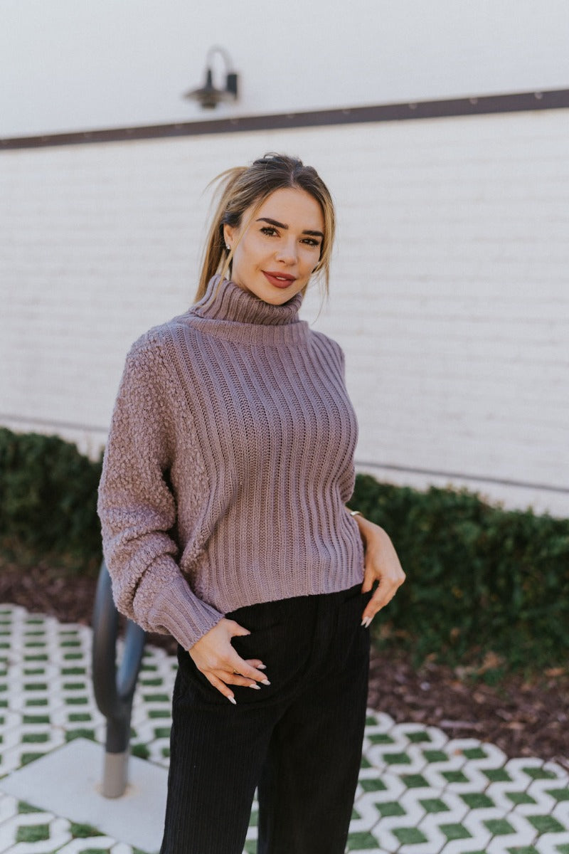 Front view of the Days Go By Sweater in Grey that features grey cable knit fabric on the front, loose turtleneck, popcorn detailing on the back and sleeves and long sleeves with cable knit wrists.