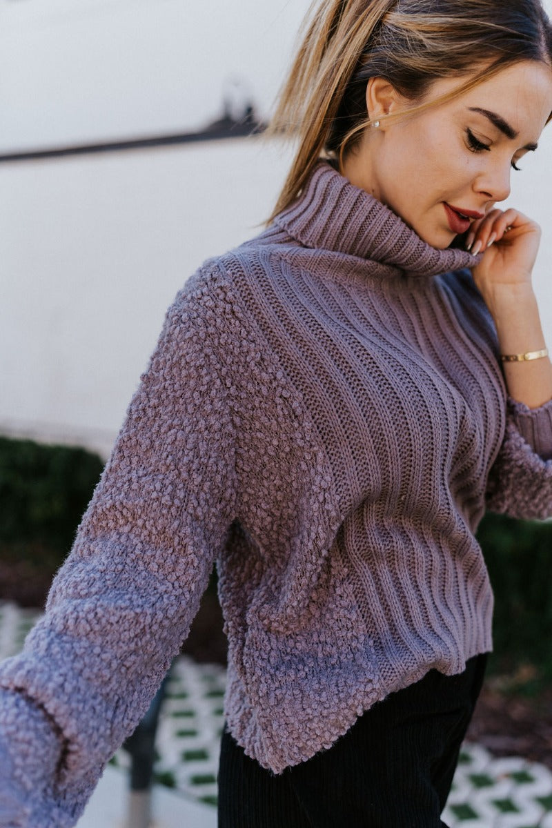 Detail view of the Days Go By Sweater in Grey that features grey cable knit fabric on the front, loose turtleneck, popcorn detailing on the back and sleeves and long sleeves with cable knit wrists.