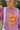 Close-up front view of model wearing the More Self Love Sweatshirt, which has a purple colored material, a round neckline with a ribbed trim, a long sleeve, a purple and orange graphic front reading "More Self Love", and side slits