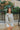 Front view of model wearing the Forever Yours Top, which has a sage green fabric , a round neckline, long sleeves, a back tie closure at the neck, and a flowy fit