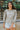 Front view of model wearing the Forever Yours Top, which has a sage green fabric , a round neckline, long sleeves, a back tie closure at the neck, and a flowy fit