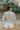 Back view of model wearing the Forever Yours Top, which has a sage green fabric , a round neckline, long sleeves, a back tie closure at the neck, and a flowy fit