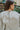 Close-up back view of model wearing the Forever Yours Top, which has a sage green fabric , a round neckline, long sleeves, a back tie closure at the neck, and a flowy fit