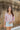Frontal view of the Cruel Summer Top that features a pink colored material, a white gingham print, a V neckline, a long ruched sleeve with adjustable ties, and a flowy fit.