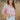 Frontal view of the Cruel Summer Top that features a pink colored material, a white gingham print, a V neckline, a long ruched sleeve with adjustable ties, and a flowy fit.