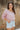 Frontal view of the Cruel Summer Top that features a pink colored material, a white gingham print, a V neckline, a long ruched sleeve with adjustable ties, and a flowy fit.