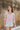 Frontal view of the Cruel Summer Top that features a pink colored material, a white gingham print, a V neckline, a long ruched sleeve with adjustable ties, and a flowy fit.
