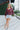 Full body front view of model wearing the Good Life Plaid Top, which has a red material with a navy plaid print, a scoop neckline, a notched neckline with an adjustable tie, a long sleeve, and a flowy fit.