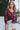 Front view of model wearing the Good Life Plaid Top, which has a red material with a navy plaid print, a scoop neckline, a notched neckline with an adjustable tie, a long sleeve, and a flowy fit.