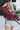 Front view of model wearing the Good Life Plaid Top, which has a red material with a navy plaid print, a scoop neckline, a notched neckline with an adjustable tie, a long sleeve, and a flowy fit.