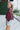 Side view of model wearing the Good Life Plaid Top, which has a red material with a navy plaid print, a scoop neckline, a notched neckline with an adjustable tie, a long sleeve, and a flowy fit.