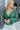 Front view of model wearing the Follow Your Heart Top, which features a green colored material, a V surplice neckline, a long sleeve, a knot detail at the waist, and a tiered ruffle bottom
