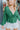 Close-up front view of model wearing the Follow Your Heart Top, which features a green colored material, a V surplice neckline, a long sleeve, a knot detail at the waist, and a tiered ruffle bottom