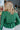 Back view of model wearing the Follow Your Heart Top, which features a green colored material, a V surplice neckline, a long sleeve, a knot detail at the waist, and a tiered ruffle bottom