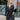 Front view of model wearing the Lost In The Moment Dress in Black, which has a black satin material, a collar neck, a surplice V neckline with a clasp closure, a long cuffed sleeve, a knot detail at the waist, and a midi length.