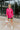 Frontal view of the Stolen Dreams Top that features a hot pink material, a collar neck and button-up front, pleated 3/4 sleeves with a bow at the wrist, and a curved bottom hem with side slits.