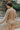 Back view of model wearing the Let's Go Top, which features a round neckline, a long sleeve, a raw curved bottom hem, and a flowy fit. Worn untucked with matching shorts.