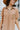 Close-up front view of model wearing the Never Better Dress, which features a camel colored material, a faux leather collar neckline, a faux leather button-up front, short sleeves, a faux leather front pocket, and a mini length.