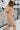Side view of model wearing the Never Better Dress, which features a camel colored material, a faux leather collar neckline, a faux leather button-up front, short sleeves, a faux leather front pocket, and a mini length.