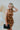 Frontal view of the Wallflower Mini Dress that features a rust silk material, a high cowl neckline, a ruched side with adjustable ties, an asymmetrical hemline, and an open back.