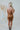 Back view of the Wallflower Mini Dress that features a rust silk material, a high cowl neckline, a ruched side with adjustable ties, an asymmetrical hemline, and an open back.
