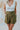 Frontal view of the Livin' The Dream Shorts that features an olive green colored material, a high-rise fit, an elastic waist, a belt detail, side pockets, and a flowy fit.