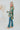 Side view of the Leave The Pieces Top that features a green silk material, a multi-colored floral print, a collar neck, a button-up front, long cuffed sleeves, a curved bottom hem, and an oversized fit.