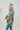 Side view of the Leave The Pieces Top that features a green silk material, a multi-colored floral print, a collar neck, a button-up front, long cuffed sleeves, a curved bottom hem, and an oversized fit.