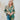 Frontal view of the Leave The Pieces Top that features a green silk material, a multi-colored floral print, a collar neck, a button-up front, long cuffed sleeves, a curved bottom hem, and an oversized fit.