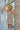Frontal view of the In Bloom Dress that features a sand colored material, a multi-colored floral print, a deep V neckline, a sleeveless design with thick straps, a side ruffle detail, a lettuce edge bottom hem, a V back, a flowy fit, and a mini length.