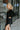Side view of the Slipped Away that features a black colored knit material, a surplice neckline, a long sleeve, ruched side detailing with adjustable strings, a side slit, a mini length, and a tight fit.