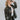 Side view of model wearing the Don't Blame Me Fringe Shacket, that is black faux-leather with a collar, a button-up front, long cuffed sleeves, fringe detailing at the chest, side pockets, and a curved hem. Worn over white tee.