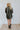 Back view of model wearing the Don't Blame Me Fringe Shacket, that is black faux-leather with a collar, a button-up front, long cuffed sleeves, fringe detailing at the chest, side pockets, and a curved hem. Worn over white tee.