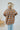 Back view of the In The Air Flannel Top that features a camel colored flannel material, a navy and white plaid pattern, a collar neck, a button-up front, two front pockets, a long cuffed sleeve, side slits, a high-low design, and an oversized fit.
