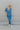 Full body front view of model wearing the Catch Up Denim Jumpsuit, that features a blue colored denim material, a collar and lapel, a surplice neckline, a short cuffed sleeve, front pockets, a button and zipper closure, side pockets, and a straight leg fi