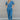 Full body front view of model wearing the Catch Up Denim Jumpsuit, that features a blue colored denim material, a collar and lapel, a surplice neckline, a short cuffed sleeve, front pockets, a button and zipper closure, side pockets, and a straight leg fi