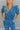 Close-up front view of model wearing the Catch Up Denim Jumpsuit, that features a blue colored denim material, a collar and lapel, a surplice neckline, a short cuffed sleeve, front pockets, a button and zipper closure, side pockets, and a straight leg fit