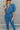 Close-up front view of model wearing the Catch Up Denim Jumpsuit, that features a blue colored denim material, a collar and lapel, a surplice neckline, a short cuffed sleeve, front pockets, a button and zipper closure, side pockets, and a straight leg fit