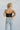 Back view of model wearing the Live Fast Top in Black, that has a black faux-leather material, a curved neckline, a bustier design with wiring through out, a back hook and clasp closure, and a cropped fit