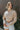 Front view of model wearing the Hit the Road Top, which has an ivory fabric with a taupe plaid pattern, a collar neck, a button-up front, long cuffed sleeves, two front pocket flaps, a cinched bottom hem with an adjustable tie, and a pleated back
