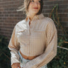 Front view of model wearing the Hit the Road Top, which has an ivory fabric with a taupe plaid pattern, a collar neck, a button-up front, long cuffed sleeves, two front pocket flaps, a cinched bottom hem with an adjustable tie, and a pleated back