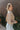 Side view of model wearing the Hit the Road Top, which has an ivory fabric with a taupe plaid pattern, a collar neck, a button-up front, long cuffed sleeves, two front pocket flaps, a cinched bottom hem with an adjustable tie, and a pleated back