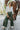 Full body front view of model wearing the Make You Mine Pants, which feature a hunter green faux-leather material, a pleated design, an elastic waist, and a wide leg fit. Worn with white top.