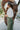 Close-up top/side view of model wearing the Make You Mine Pants, which feature a hunter green faux-leather material, a pleated design, an elastic waist, and a wide leg fit. Worn with white top.
