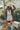 Front view of model wearing the Take Me Home Plaid Shacket, which has a rust  material with plaid, a collar, a button-up front, two front pockets, long cuffed sleeves, side slits, and an oversized fit. Worn with white brami and shorts.