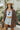 Front view of model wearing the Take Me Home Plaid Shacket, which has a rust  material with plaid, a collar, a button-up front, two front pockets, long cuffed sleeves, side slits, and an oversized fit. Worn with white brami and shorts.