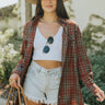 Front view of model wearing the Take Me Home Plaid Shacket, which has a rust  material with plaid, a collar, a button-up front, two front pockets, long cuffed sleeves, side slits, and an oversized fit. Worn with white brami and shorts.