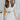 Frontal view of the Heart Breaker Sweater Dress that features an ivory knit material, a turtleneck, a sleeveless design, and a mini length. Dress is belted.